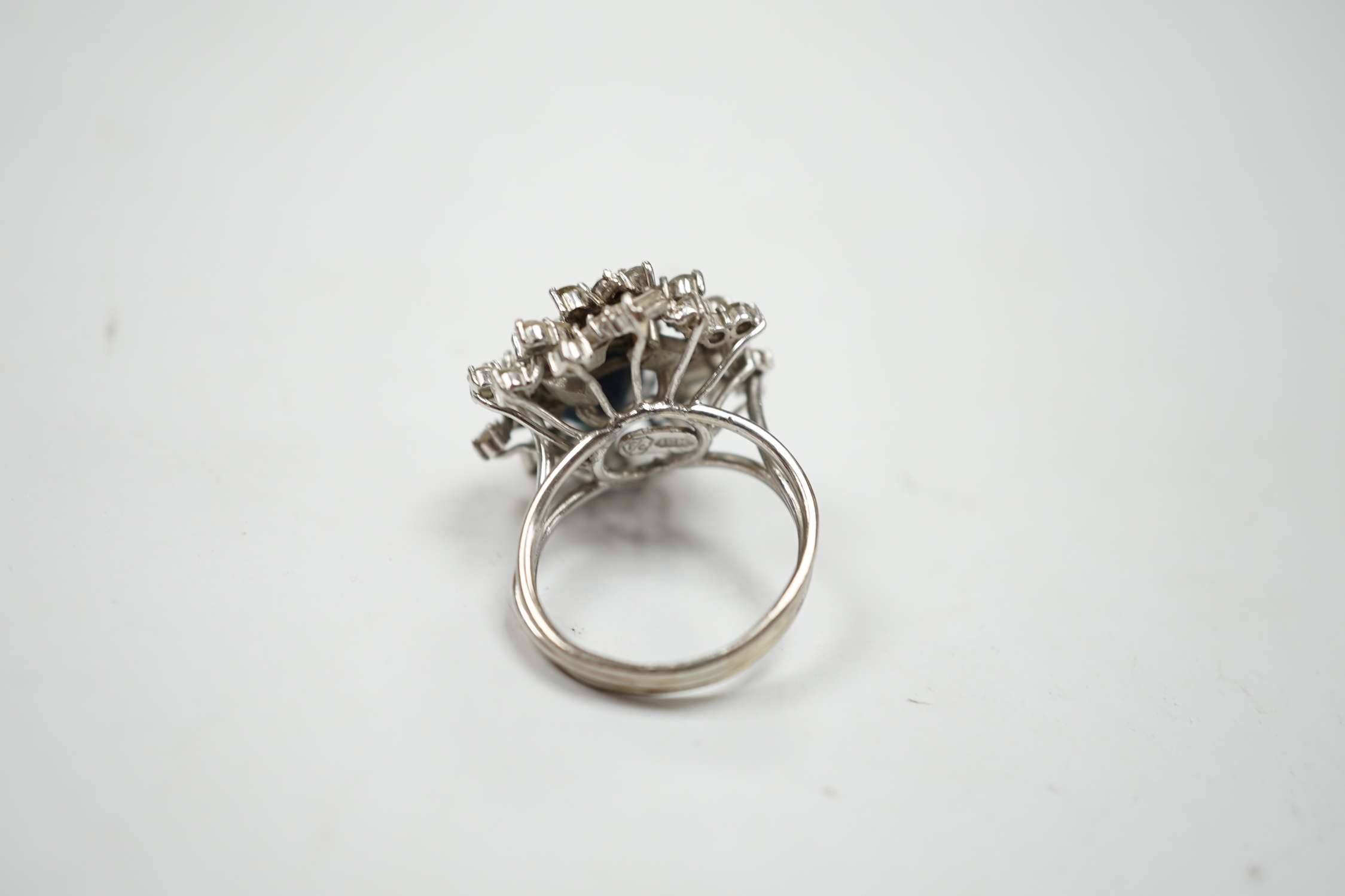 A mid to late 20th century 18k white metal, single stone oval cut sapphire and baguette and round cut diamond cluster set dress ring, size M/N, gross weight 10.3 grams.